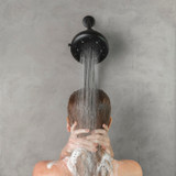 A woman using Nebia Corre Four-Funtion Fixed Showerhead Matte Black spraying water in a gray bathroom