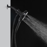 Side view of the Nebia Corre Four-Function Handshower Matte Black spraying water with a gray and black background